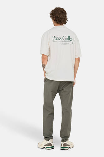 Wit T-shirt met korte mouwen van ONLY & SONS, met groene "Parks Gallery" tekst op de rug, gedragen met kaki broek en crèmekleurige sneakers.

