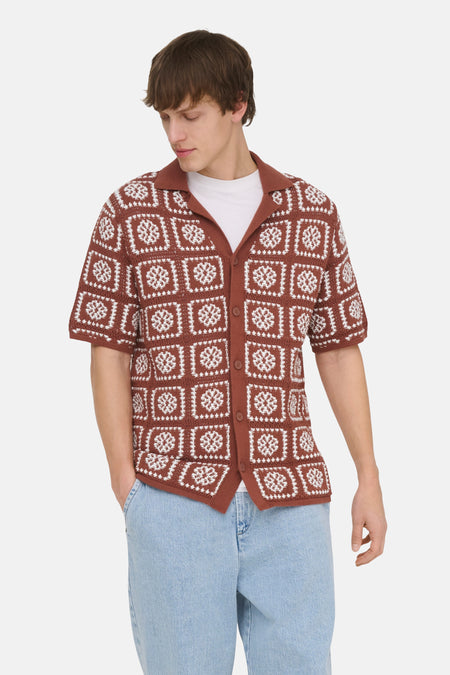 Bruine gebreide pull met korte mouwen van ONLY & SONS®, met witte bloempatronen, gedragen met een wit T-shirt en lichte spijkerbroek.