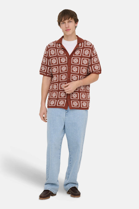 Bruine gebreide pull van ONLY & SONS met witte vierkante motieven, kraag en korte mouwen, gedragen over een wit T-shirt en lichte jeans.