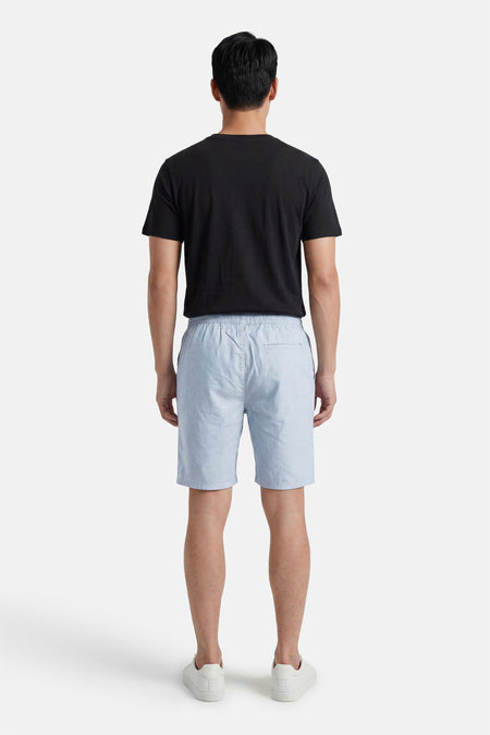 Achterkant van lichtblauwe short van ONLY & SONS® van gestructureerde stof, met elastische tailleband, gedragen met een zwart T-shirt en witte sneakers.
