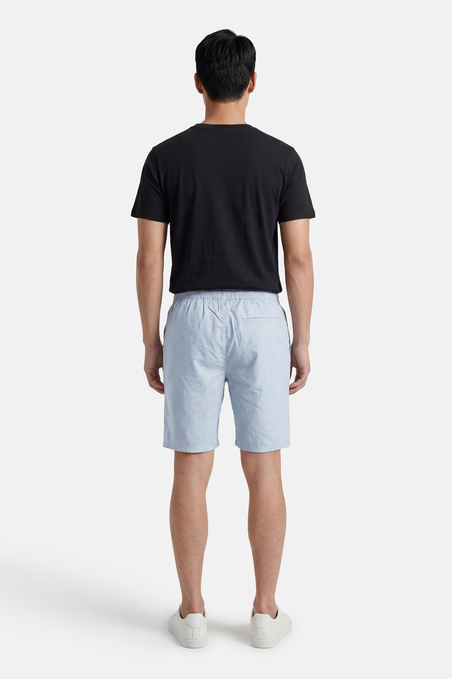 Achterkant van lichtblauwe short van ONLY & SONS® van gestructureerde stof, met elastische tailleband, gedragen met een zwart T-shirt en witte sneakers.