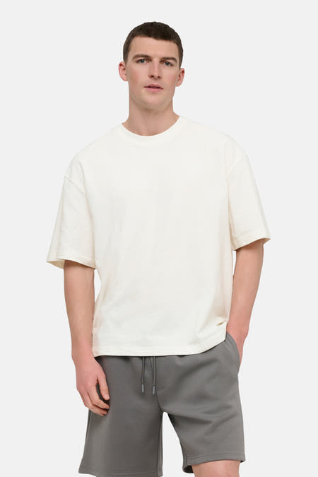 T-shirt blanc à manches courtes ONLY & SONS®, porté avec un short gris et des baskets blanches avec chaussettes.