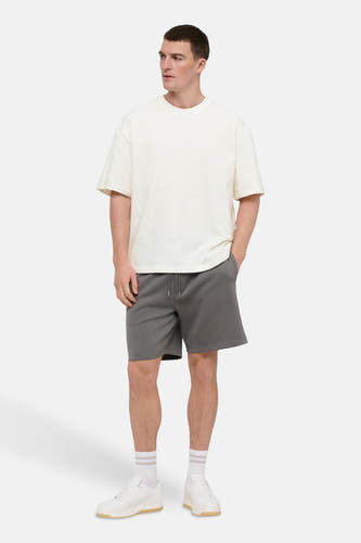 Wit T-shirt met korte mouwen van ONLY & SONS®, gedragen met grijze shorts en witte sneakers met sokken.