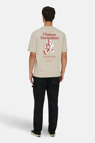 Ecru T-shirt met korte mouwen van ONLY & SONS®, met rode 'Cinéma Surréaliste' print op de rug, gedragen met een zwarte broek en sneakers.
