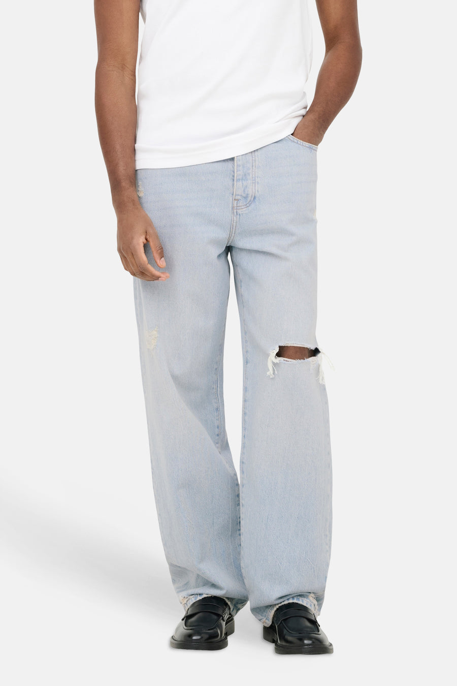 Lichtblauwe wide-leg jeans van ONLY & SONS met gerafelde details en gescheurde knie, gedragen met een wit T-shirt en zwarte loafers.
