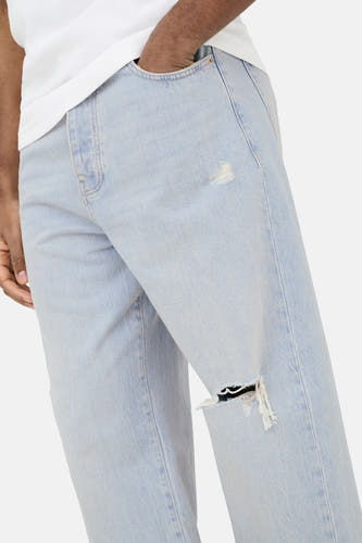 Lichtblauwe wijde denim jeans van ONLY & SONS® met scheuren, een hand in de zak en een wit T-shirt.