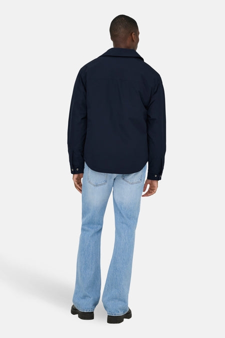 Persoon van achteren gezien, marineblauwe jas, blauwe spijkerbroek, zwarte schoenen.