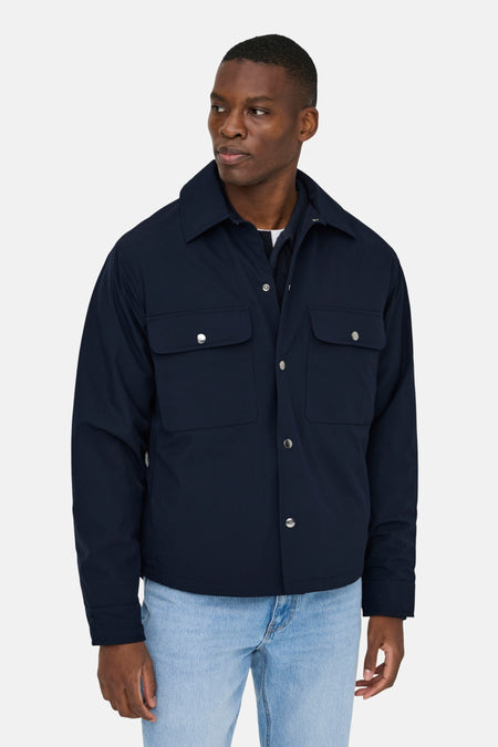 Man in blauwe jas met zilveren knopen en lichte jeans.