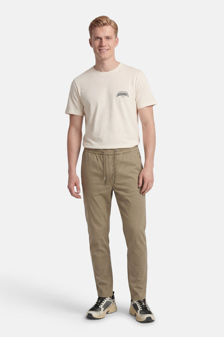 Beige broek van ONLY & SONS, met trekkoord, gecombineerd met een crèmekleurig T-shirt en sportschoenen.