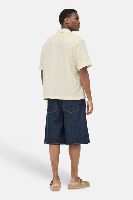 Ecru kortemouwenhemd van ONLY & SONS® met crêpe-achtige textuur, achterkant zichtbaar op man met donkerblauwe denim shorts en beige sandalen.