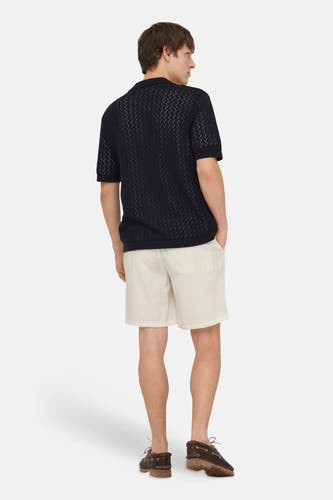 Ecru short van ONLY & SONS, gecombineerd met een zwart poloshirt met patroon en bruine bootschoenen.