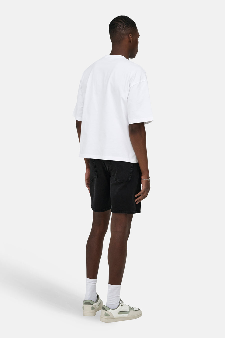 Short en jean noir en denim de ONLY & SONS, vu de dos, associé à un t-shirt blanc, des chaussettes blanches et des baskets de couleur crème.
