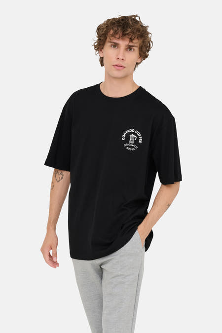 Zwart T-shirt met korte mouwen van ONLY & SONS®, met witte opdruk en gedragen met een grijze broek.
