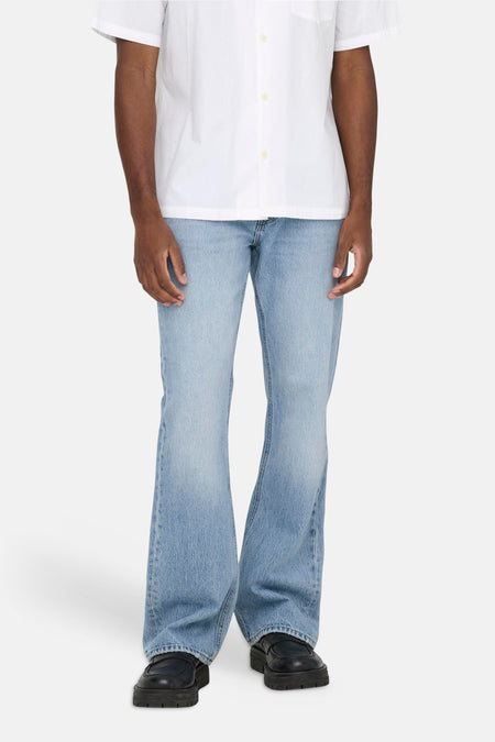 Jean bootcut bleu clair en denim de ONLY & SONS, avec une main dans la poche et une chemise blanche.