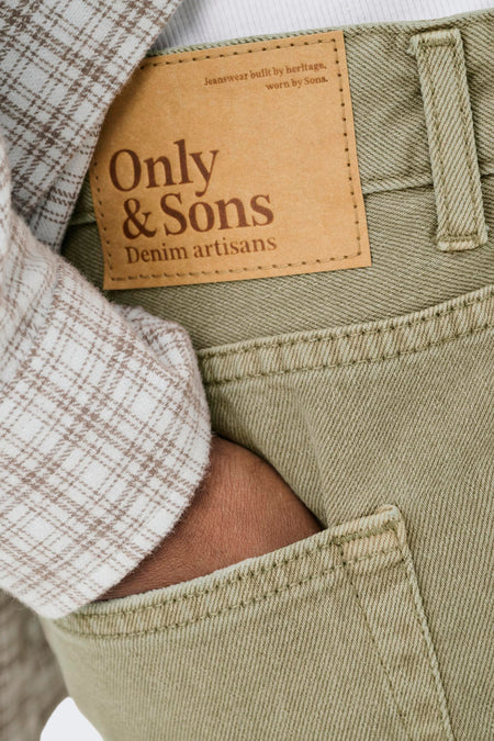 Short en jean de couleur beige de ONLY & SONS avec une étiquette de marque marron sur la poche arrière et une manche de chemise à carreaux.