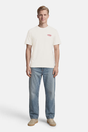 T-shirt de couleur crème de ONLY & SONS® avec petit imprimé rouge sur la poitrine, porté avec un jean bleu et des baskets beiges.