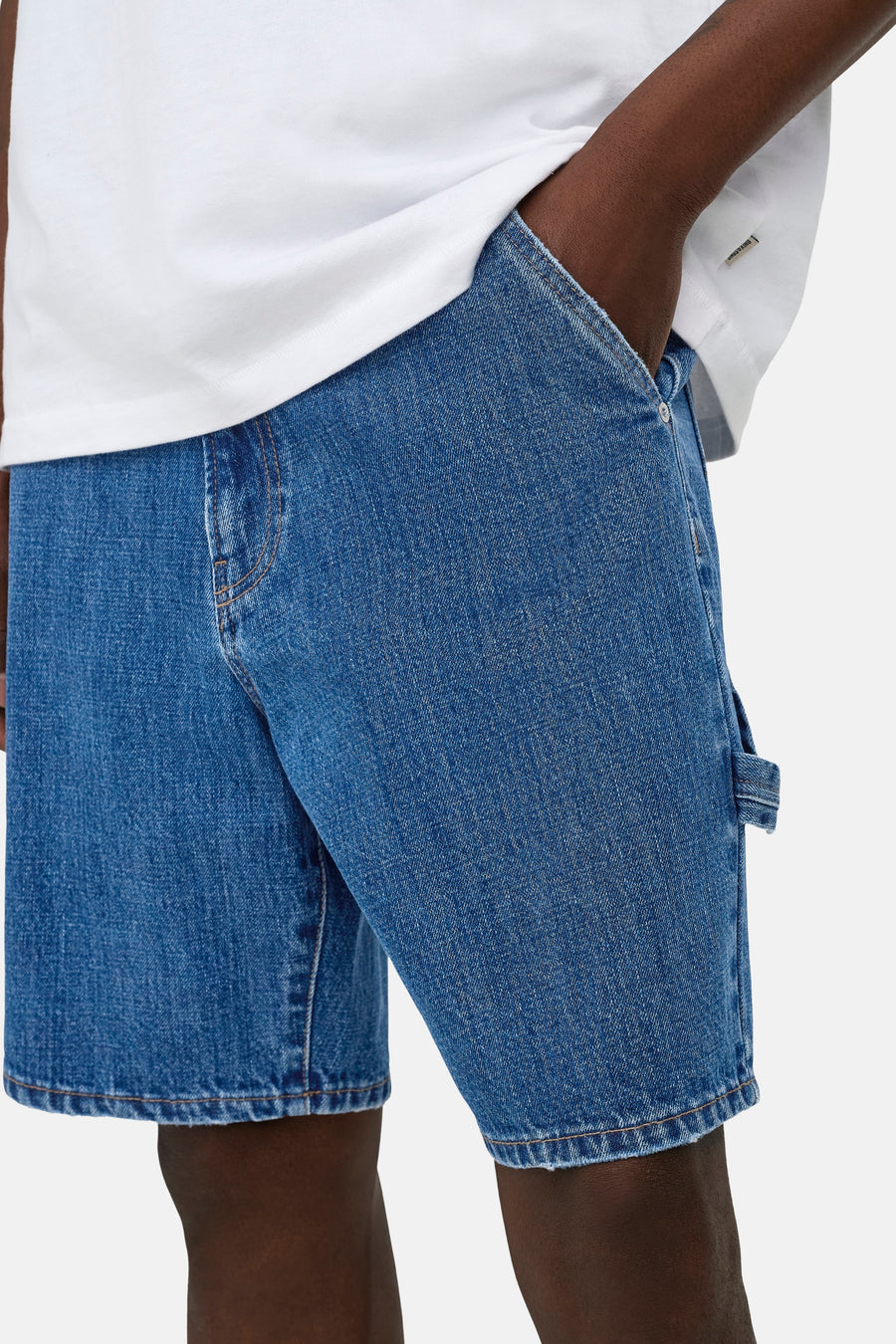 Short en jean bleu moyen ONLY & SONS® avec passant de marteau, porté avec un t-shirt blanc et une main dans la poche.