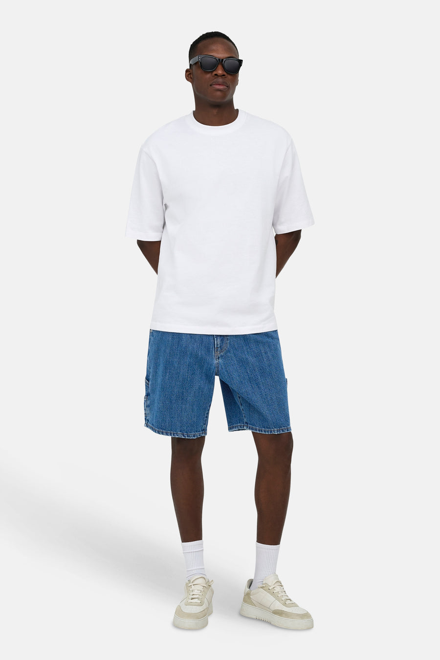 Short en jean bleu moyen de ONLY & SONS®, avec détail de poche latérale, porté par un mannequin avec un t-shirt blanc, des lunettes de soleil et des baskets claires.