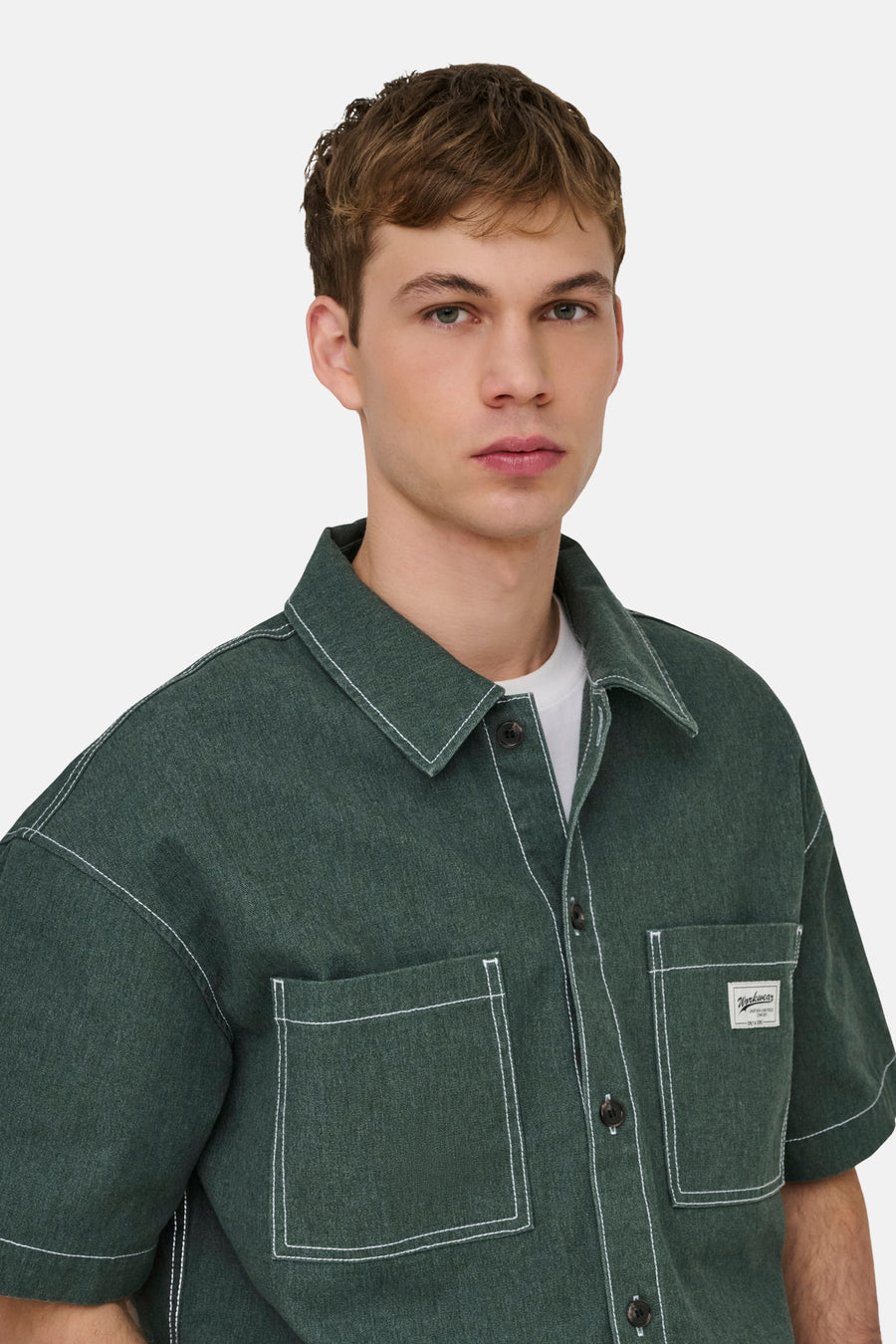 Groen hemd met korte mouwen van ONLY & SONS® met witte stiksels en borstzakken, gedragen door een man.