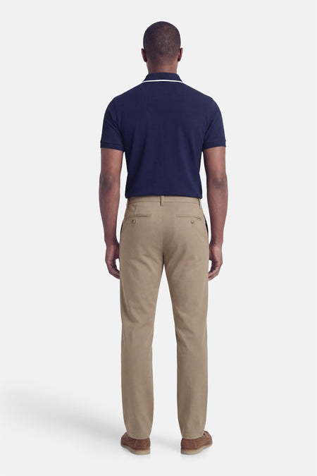 Beige broek van ONLY & SONS, met knoopdetail op de achterzakken, gedragen met een donkerblauw poloshirt en bruine schoenen.
