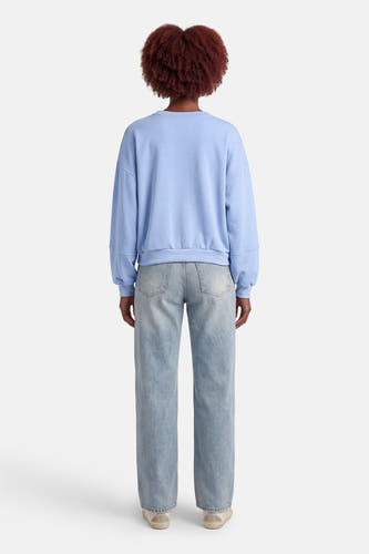 Blauwe sweater met ronde hals van Terra di Siena, gezien van achteren, gecombineerd met lichtblauwe jeans en lage sneakers.