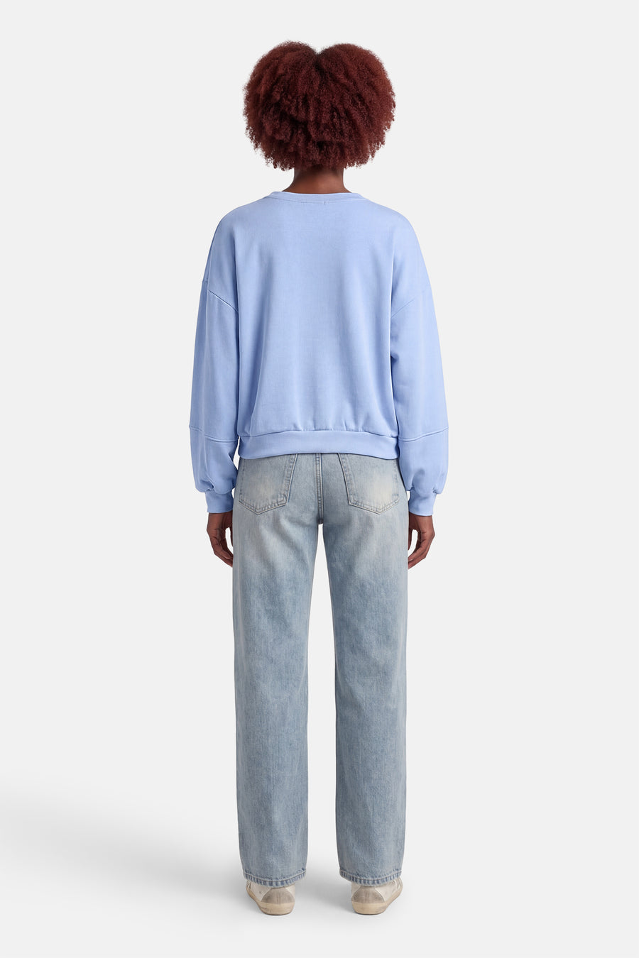 Blauwe sweater met ronde hals van Terra di Siena, gezien van achteren, gecombineerd met lichtblauwe jeans en lage sneakers.