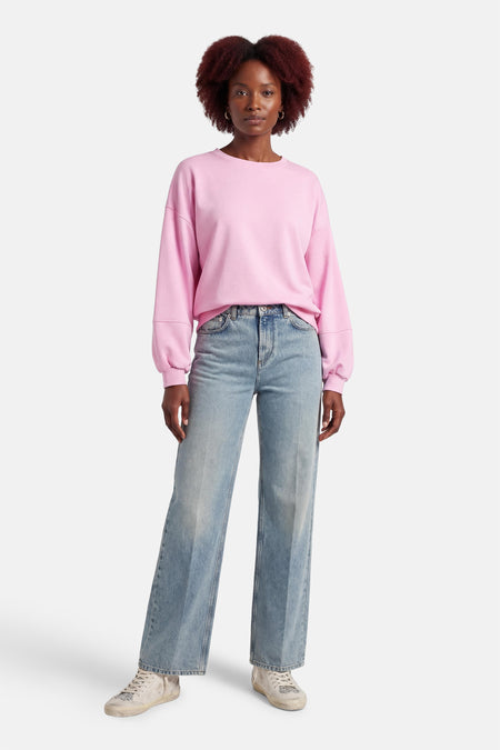 Pull rose de Terra di Siena, à manches longues, porté avec un jean ample et des baskets.