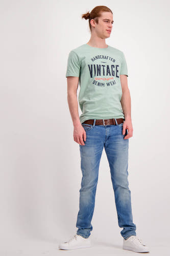 Bruine riem van Levi's® Accessories, gedragen met een lichtblauwe jeans en een lichtgroen T-shirt, gecombineerd met witte sneakers.
