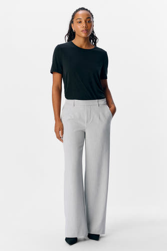 Pantalon gris d'OBJECT, avec des jambes qui s'évasent et porté avec un t-shirt noir et des chaussures noires.