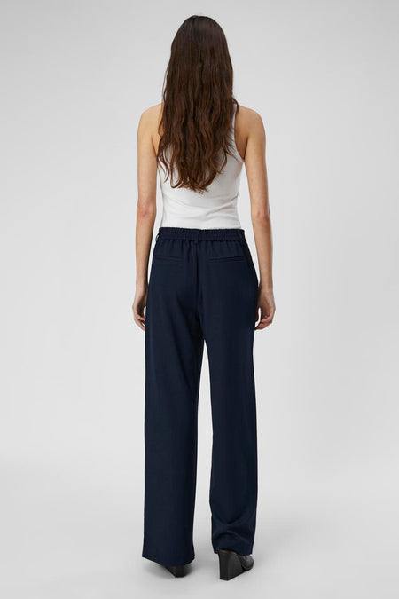 Blauwe broek van OBJECT, gezien van achteren, met een elastische tailleband en gedragen met een witte tanktop en zwarte schoenen.
