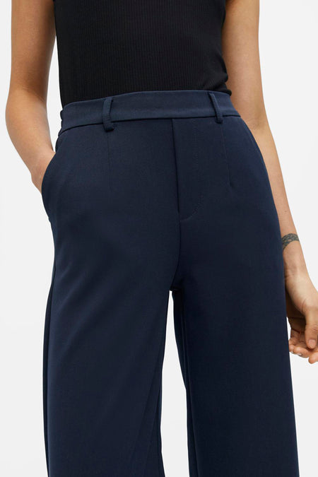 Pantalon bleu d'OBJECT, avec des jambes larges et une main dans la poche.