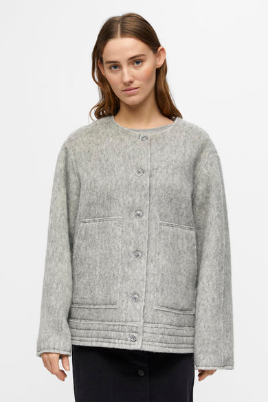 Manteau court gris d'OBJECT, avec une finition brodée et porté sur une longue jupe sombre.