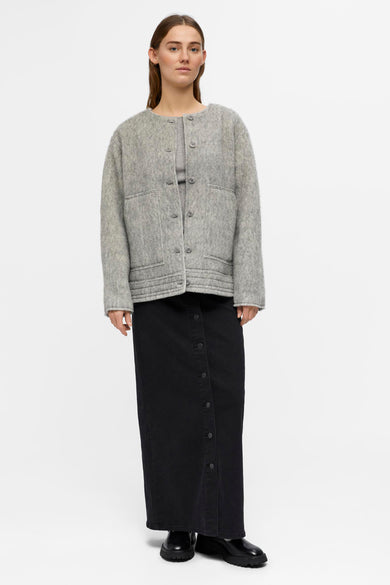 Manteau court gris d'OBJECT, avec fermeture à boutons et poches brodées, porté avec une jupe noire à boutons.