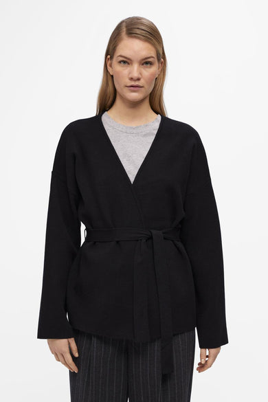 Gilet noir d'OBJECT, avec une ceinture à la taille, porté sur un pantalon rayé et des bottes noires.