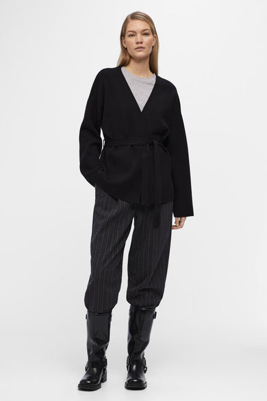 Gilet noir d'OBJECT avec ceinture à carreaux, porté sur une chemise grise et un pantalon rayé, avec des bottes noires.