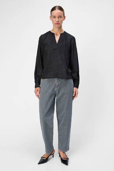 Zwarte blouse met lange mouwen van OBJECT, met een V-hals en gedragen met blauwe jeans en zwarte hakken.
