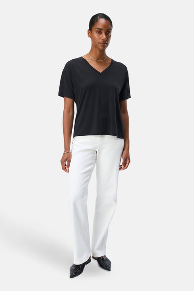T-shirt noir à manches courtes d'OBJECT, avec un col V, porté avec une chaîne en argent et des jeans blancs.
