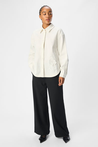 Ecru hemd met lange mouwen van OBJECT, met geborduurde florale details en gedragen met een zwarte pantalon.
