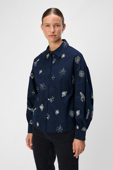 Blauw overhemd met lange mouwen van OBJECT, met witte borduursels van bladeren, ogen, sterren en vogels.
