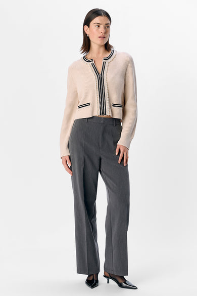 Gilet écru d'OBJECT, terminé avec des perles le long de la fermeture éclair et porté avec un pantalon gris et des chaussures noires.