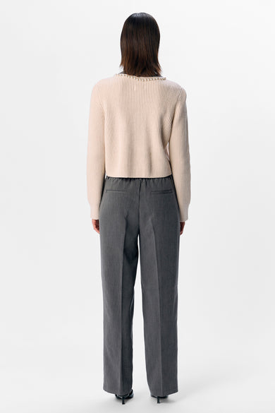 Gilet écru d'OBJECT avec des détails de perles le long de la ligne du cou, associé à un pantalon gris et des talons noirs, vu par derrière.