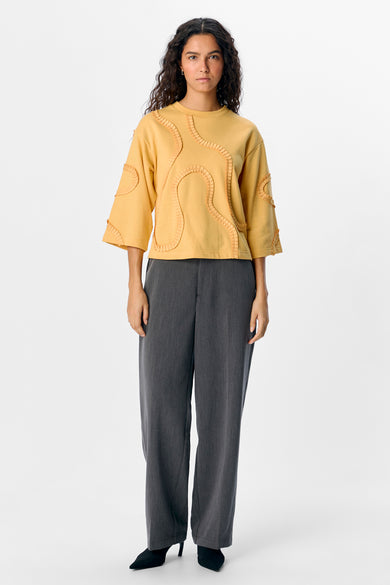 Gele sweater van OBJECT, met decoratieve plooien, gecombineerd met een grijze pantalon en zwarte schoenen.
