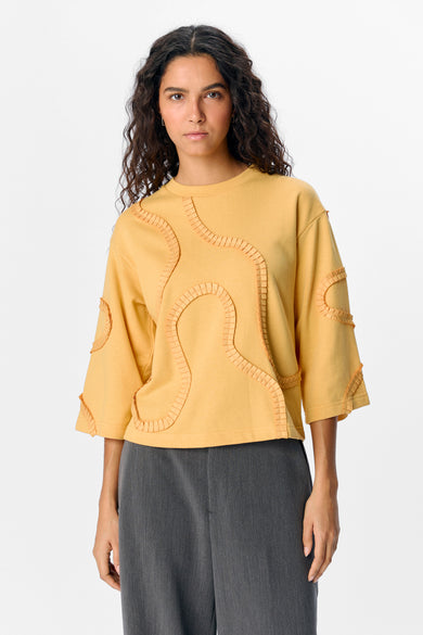 Gele sweater van OBJECT, met decoratieve applicaties en gecombineerd met grijze broek.
