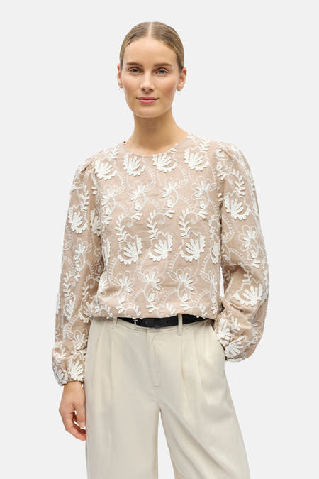 Blouse beige à longues manches d'OBJECT, avec des motifs floraux brodés et des manches bouffantes, portée avec une jupe crème et des chaussures noires.