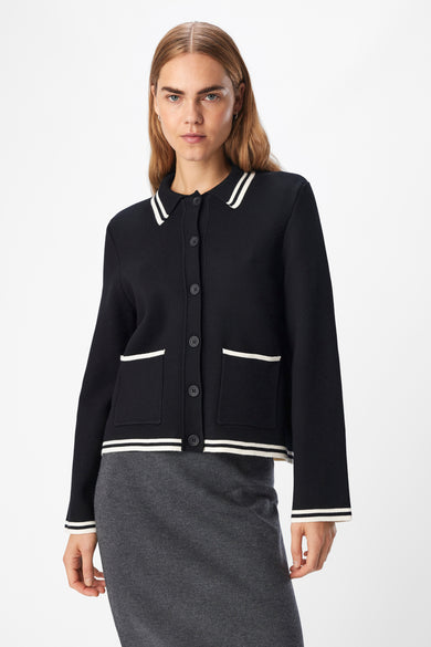 Cardigan noir d'OBJECT avec une bordure blanche, associé à une jupe grise avec une fente et des bottes noires, vu de dos.