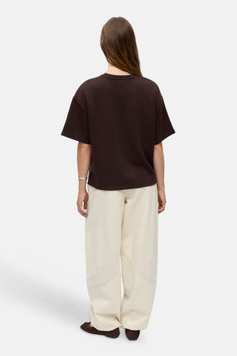 Bruine oversized sweater van OBJECT, achterkant weergegeven, met ronde hals en korte mouwen, gedragen met crèmekleurige broek en bruine slippers.