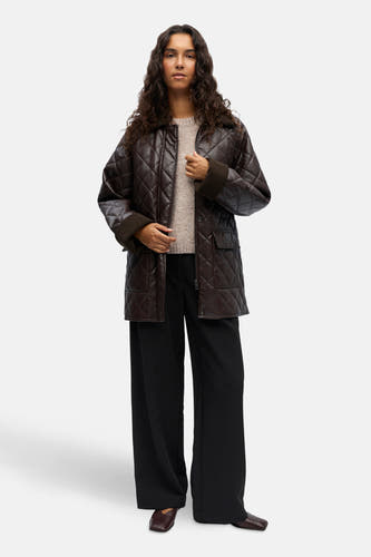 Manteau court brun d'OBJECT, avec un motif brodé en forme de lunettes, associé à une chemise beige et à un pantalon noir ample.