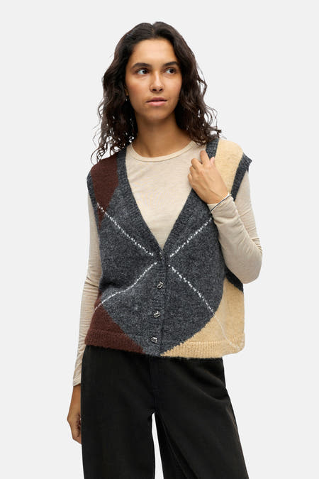 Grijs gilet van OBJECT met argyle ruitpatroon, gedragen over een beige shirt met lange mouwen en een zwarte broek.
