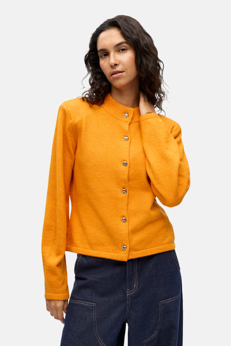 Oranje gilet van OBJECT met lange mouwen en zilverkleurige knopen, gedragen met een donkerblauwe jeans.
