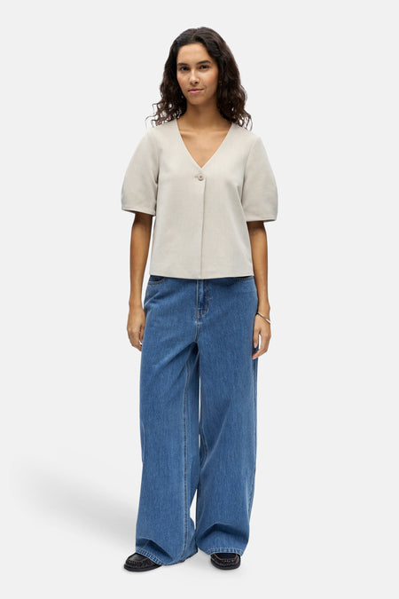 Gilet écru de OBJECT, avec fermeture à boutons, manches courtes et combiné avec un jean bleu large et des chaussures noires.
